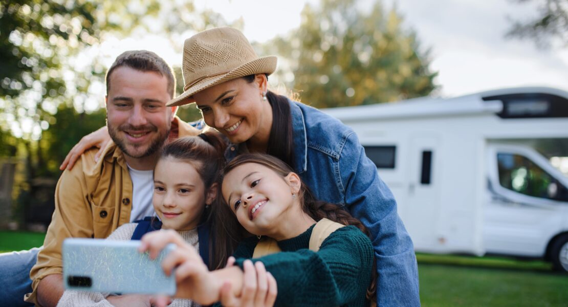 Family of 4 taking picture on a phone in front of their motorhome